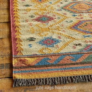 May include: A handwoven jute rug with a geometric pattern in shades of yellow, red, blue, and brown. The rug has a fringe border and the text "jute rugs handloom" is visible at the bottom.