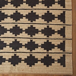 May include: A brown and black geometric patterned rug with a woven texture. The rug has a simple design with repeating geometric shapes.