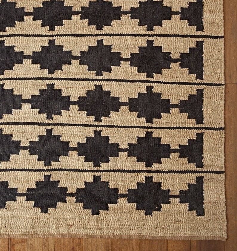 May include: A brown and black geometric patterned rug with a woven texture. The rug has a simple design with repeating geometric shapes.