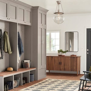May include: A gray entryway with a wooden bench, two sets of cabinets, a wooden cabinet with two doors, a black framed mirror, and a glass globe pendant light.