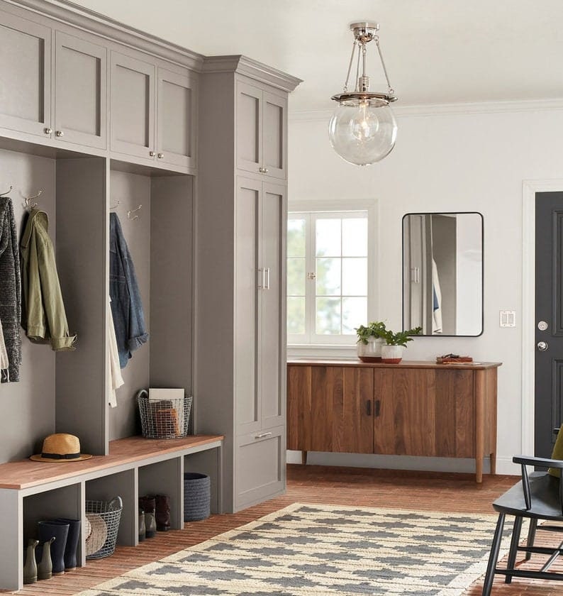 May include: A gray entryway with a wooden bench, two sets of cabinets, a wooden cabinet with two doors, a black framed mirror, and a glass globe pendant light.