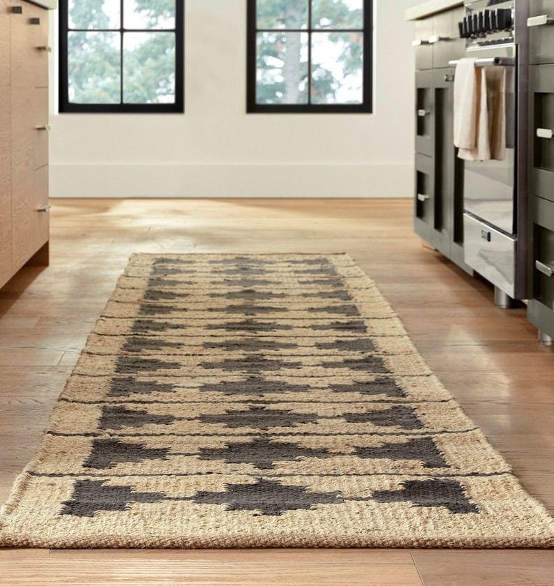 May include: A brown and black patterned jute rug runner with a geometric design. The rug is placed on a wooden floor in a kitchen.