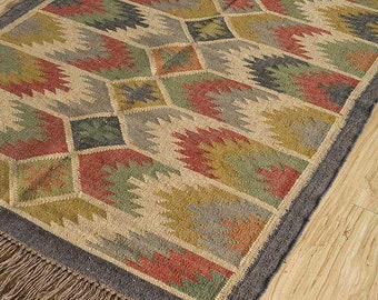 May include: Rectangular jute rug with a geometric pattern in shades of red, green, yellow, and gray. The rug has a dark gray border and fringe along the edges. The rug is placed on a light brown wooden floor.