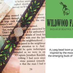 May include: A green, black and white beaded bracelet with a leather strap. The bracelet is on a book with text that reads "WILDWOOD FAYRE BAZAAR OF BEAUTIFUL THINGS" and "A j-peg bead loom pattern inspired by the moon and the emerging buds of spring."