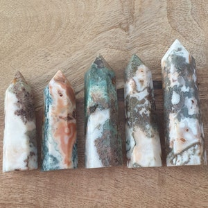 Peut inclure: Six pointes de cristal d'agate polies avec une variété de motifs bruns, blancs et verts. Les pointes sont disposées en rangée sur une surface en bois.