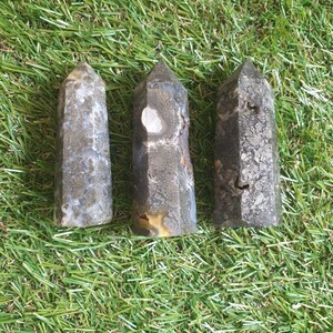 Peut inclure: Trois pointes de cristal d'agate gris et blanc avec une surface rugueuse et texturée. Les pointes sont disposées en rangée sur une surface verte.