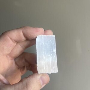 Könnte beinhalten: Ein rechteckiger, durchscheinend weißer Selenitkristall. Der Kristall hat eine raue, natürliche Textur. Der Selenit scheint ein natürliches Mineralexemplar zu sein.