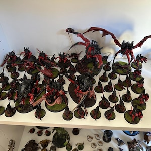 Könnte beinhalten: Eine Sammlung von Miniatur-Tabletop-Spielfiguren, die in Schwarz und Rot bemalt sind. Das Set enthält verschiedene insektenartige Kreaturen, darunter ein großes geflügeltes Monster, die alle auf runden Sockeln mit grünen, texturierten Bodendetails stehen.