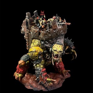 Puede incluir: Figura en miniatura detallada de una criatura monstruosa con cuerpo amarillo y verde, pelaje rojo y rostro amenazante. La criatura lleva una plataforma con varias figuras más pequeñas. La figura está sobre un fondo negro.