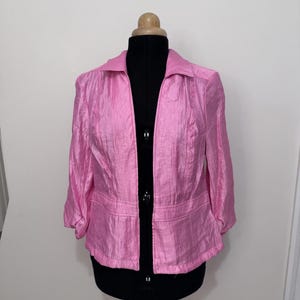 May include: A pink jacket with a collar and three-quarter sleeves. The jacket is displayed on a black mannequin. The fabric has a textured appearance. The jacket is open in the front.