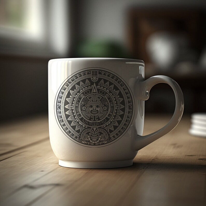 Puede incluir: Taza de cer&aacute;mica blanca con un dise&ntilde;o en blanco y negro de un calendario azteca circular con una cara en el centro.