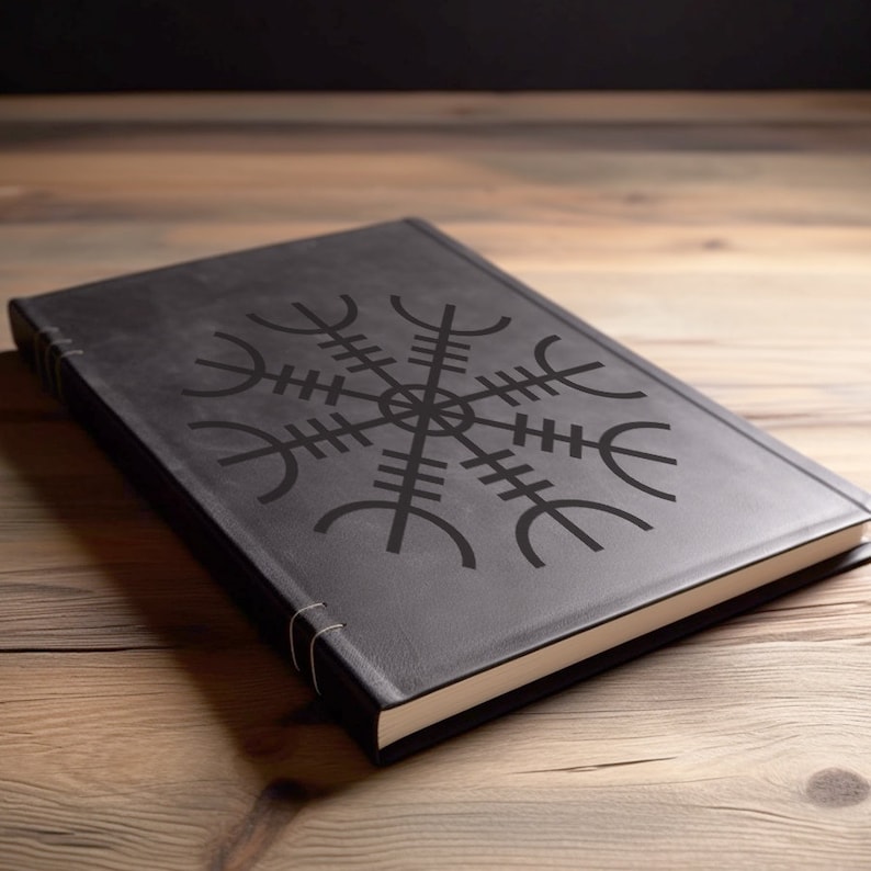May include: A black leather-bound journal with a Vegvisir symbol on the cover. The journal is closed and lying on a wooden surface.