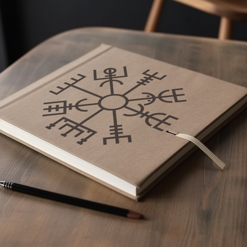 May include: A brown leather-bound journal with a compass symbol on the cover. The journal has a white ribbon bookmark and is lying on a wooden table.