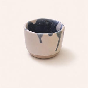 Peut inclure: Une petite tasse en céramique faite à la main avec un extérieur crème et un intérieur bleu foncé. La peinture bleue dégouline sur les côtés de la tasse. La base de la tasse est de couleur beige clair. Cette tasse est idéale pour les petits objets.