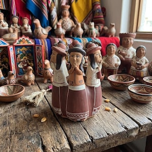 Könnte beinhalten: Eine Terrakotta-Skulptur mit drei miteinander verbundenen Figuren, die jeweils einen Hut und einen langen Rock mit weißen Bemalungen tragen. Die Figuren halten ihre Hände vor der Brust gefaltet und stehen auf einer verwitterten Holzoberfläche.