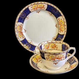 Könnte beinhalten: Ein Vintage-Teetassen- und Untertassen-Set mit einem floralen Muster in Gelb-, Orange- und Blautönen. Das Set verfügt über ein zartes Blumenmuster mit goldenen Akzenten.