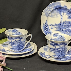 Könnte beinhalten: Ein Set aus blauen und weißen Teetassen und Untertassen mit einem Cottagecore-Design. Die Tassen und Untertassen haben ein blaues und weißes Blumenmuster mit einer Cottage-Szene.