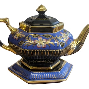 Könnte beinhalten: Eine blaue und schwarze Keramik-Teekanne mit goldenen Akzenten. Die Teekanne hat florale Designs und einen goldenen Griff und Ausguss. Der Deckel ist schwarz mit einer goldenen Spitze, und der Sockel ist blau und schwarz.