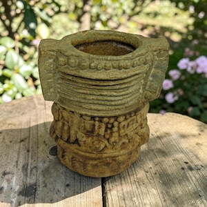 May include: A cylindrical ceramic vessel with a textured, earthy olive-green glaze. The exterior features horizontal bands of raised decorative patterns, including small spheres and linear ridges, with two protruding side handles near the rim.