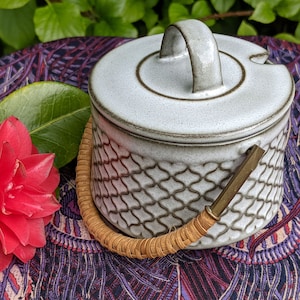 Può includere: Zuccheriera in ceramica bianca con coperchio e manico intrecciato. La ciotola presenta un motivo geometrico e una glassa marrone.