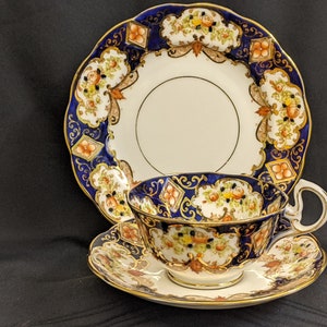 Könnte beinhalten: Ein blaues und goldenes Tee-Set mit floralen Mustern. Die Teetasse hat einen Henkel und die Untertasse einen gewellten Rand.