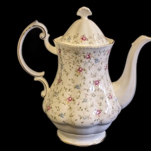 Peut inclure: Une cafetière en porcelaine blanche avec un motif floral. La cafetière a un couvercle avec un bouton décoratif et une bordure dorée autour du bord.