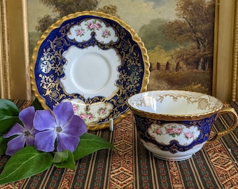 May include: A vintage teacup and saucer set with a blue and gold floral design. The cup and saucer have a white background with gold trim and a floral pattern in pink and white.