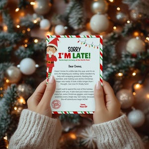 Op de afbeelding: Een rechthoekig briefje met een rood-groen gestreepte rand met een illustratie van een elf en de tekst SORRY I'M LATE! Santa kept me busy at the North Pole! Dear Emma, Oops! I know I'm a little late this year, and I'm so sorry for keeping you waiting.
