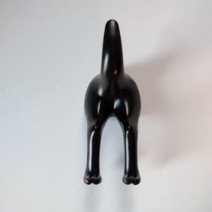May include: A glossy black decorative object, shaped like the rear end of a dog, with two legs and a tail. The object is set against a white background, creating a striking contrast.