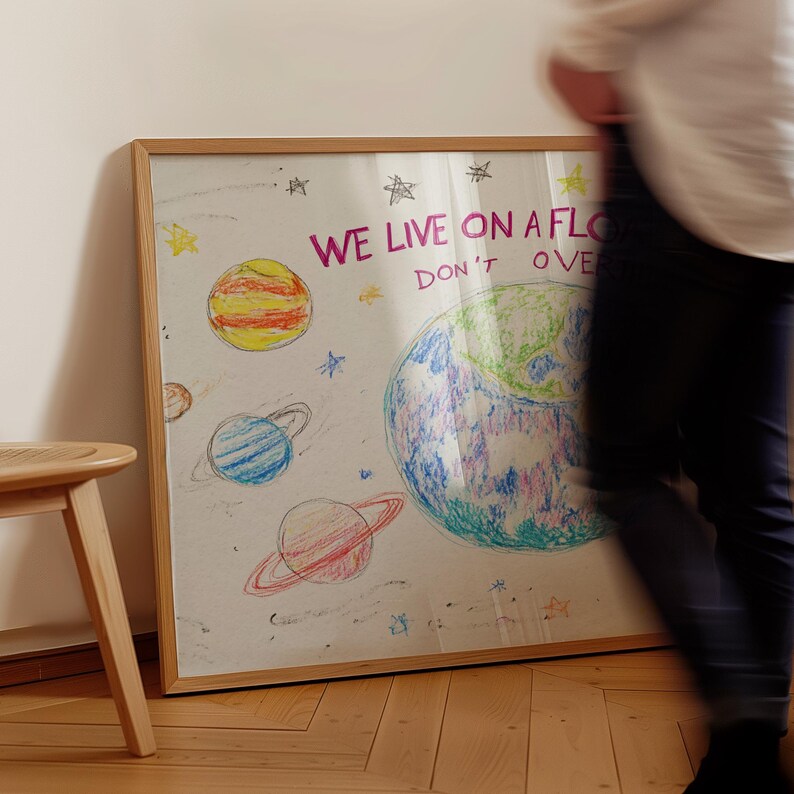 May include: A framed drawing of a colorful planet with stars and planets around it. The drawing is on a white background and has the text "WE LIVE ON A FLOATING ROCK DON'T OVERTHINK IT" in pink letters.