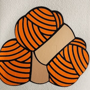 May include: A graphic illustration of three orange yarn balls with black outlines, arranged together. The yarn balls are on a white background. The illustration has a tan-colored band around the yarn balls.
