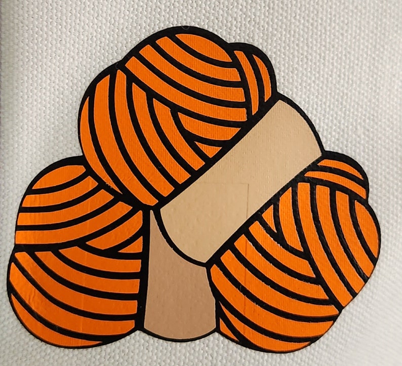 May include: A graphic illustration of three orange yarn balls with black outlines, arranged together. The yarn balls are on a white background. The illustration has a tan-colored band around the yarn balls.