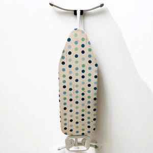 May include: An ironing board with a cream-colored cover featuring a pattern of blue and green polka dots. The board is mounted on a white wall with a silver-colored bracket.