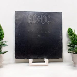 May include: A black vinyl record with the band AC/DC's logo and the album title "Back in Black" printed in white. The record is displayed on a white record stand.