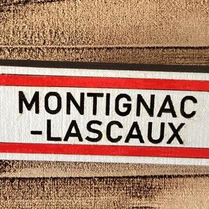 Puede incluir: Un llavero de metal plateado con una etiqueta rectangular roja y negra que dice "MONTIGNAC - LASCAUX".
