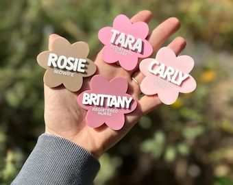 May include: Four pink and brown flower-shaped name tags with white text. The tags read "Rosie Midwife", "Tara Registered Nurse", "Brittany Registered Nurse", and "Carly Enrolled Nurse".