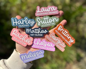 以下が含まれることがあります： 「Laura Registered Midwife」や「Harley Teacher」など、さまざまな職業と名前が書かれたカラフルなネームバッジのコレクション。 ピンク、青、緑、オレンジなどの色があります。