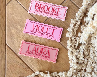 May include: Three pink name tags with white scalloped edges and red text. The name tags read "Brooke Registered Nurse", "Violet Registered Nurse", and "Laura Registered Nurse".