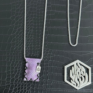 Puede incluir: Collar de cadena plateada con un colgante de cuero morado y un pequeño dije plateado. También se ve una segunda cadena plateada. También hay un colgante geométrico plateado con un diseño de llama.