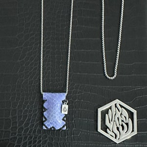 Puede incluir: Dos cadenas de plata con colgantes. Un colgante es una pieza rectangular de piedra morada con un dije de plata. El otro colgante es un hexágono de plata con un diseño recortado.