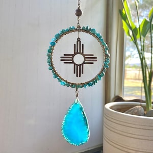 May include: A turquoise and gold sun symbol dreamcatcher with a turquoise agate pendant. The dreamcatcher is made with small turquoise stones and a wire frame. The pendant is a teardrop shape with a rough edge.