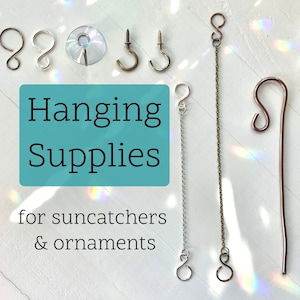 May include: Assortment of hanging supplies for suncatchers and ornaments, including silver and gold jump rings, a suction cup, a silver chain, a silver hook, a gold hook, a silver wire loop, and a copper wire loop.