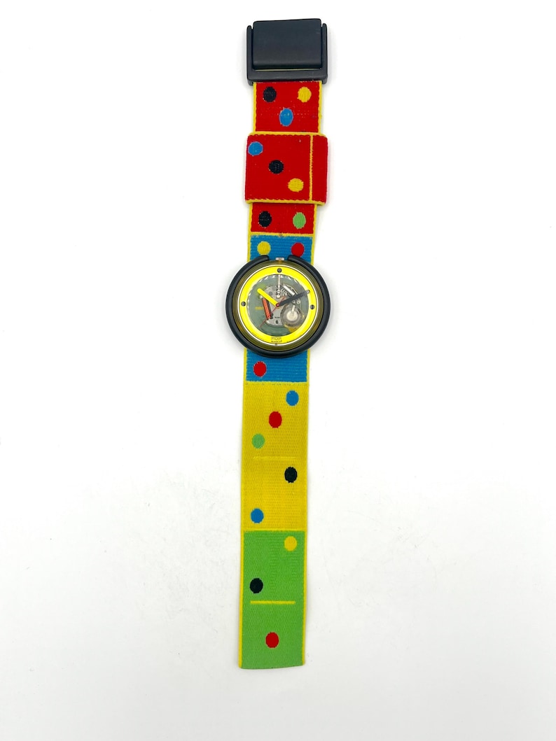 May include: A colorful wristwatch with a domino-themed band. The band features red, yellow, and green sections with polka dots. The watch face is black with a yellow border and a detailed dial.