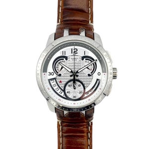 Op de afbeelding: Een zilverkleurig Swatch-horloge met een witte wijzerplaat en een bruine leren band. De wijzerplaat heeft zwarte en witte subwijzerplaten, een datumweergave en het Swatch-logo. Het horloge heeft een ronde kast en een leren band.