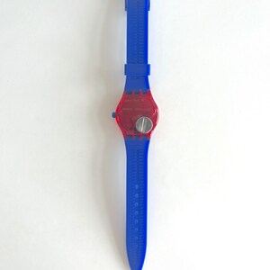 Peut inclure: Une montre-bracelet bleue et rouge avec un cadran rouge transparent. La montre a un bracelet bleu avec un motif textur&eacute; et un cadran argent&eacute;. La montre est de style classique.