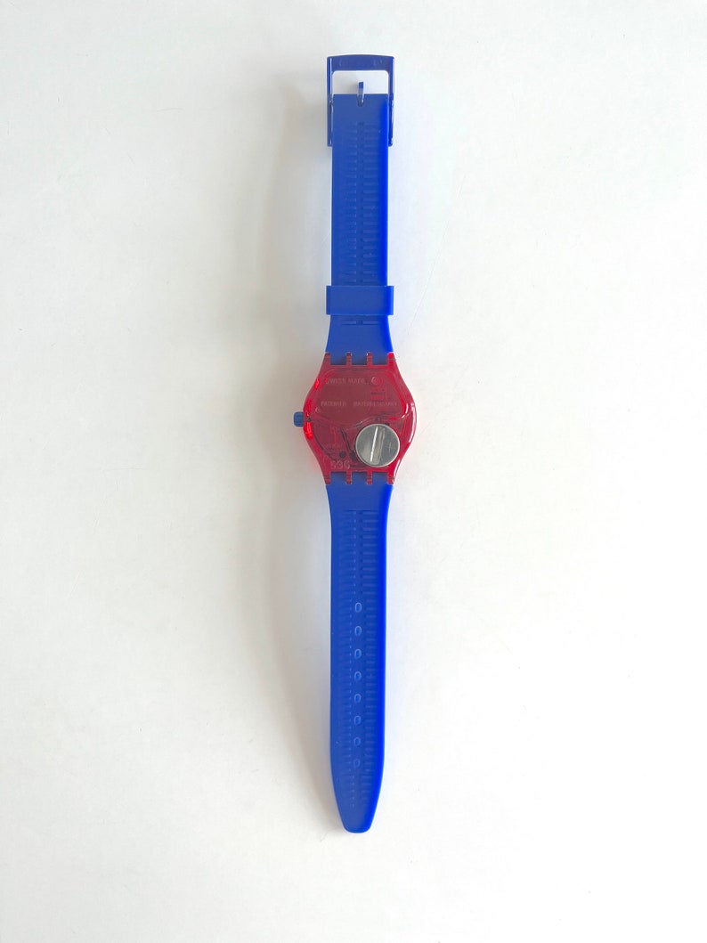 Peut inclure: Une montre-bracelet bleue et rouge avec un cadran rouge transparent. La montre a un bracelet bleu avec un motif textur&eacute; et un cadran argent&eacute;. La montre est de style classique.