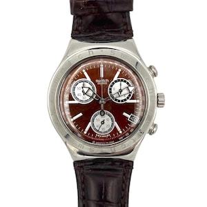 May include: A Swatch chronograph watch with a brown dial and a stainless steel case. The watch features three sub-dials, a date window, and a brown leather strap. The watch has a seconds hand and is water resistant.