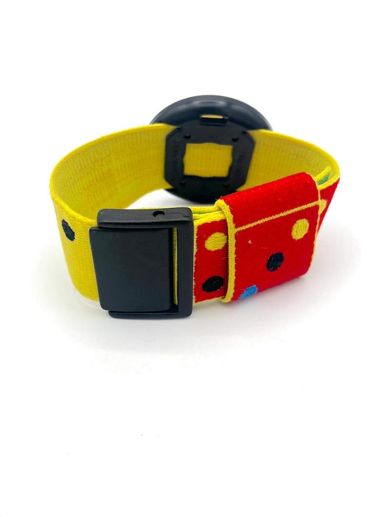 May include: A colorful watch with a yellow strap and a black watch face. The strap features a red section with polka dots and a black buckle. The watch is designed with a playful and vibrant aesthetic.