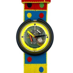 May include: A Swatch POP watch with a black case and a yellow dial. The watch band is yellow, blue, and red with polka dots. The watch face has the text "POP Swatch".