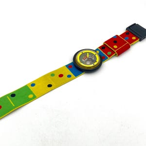 May include: A colorful wristwatch with a patterned band. The band features a yellow, green, and red design with polka dots and domino-like patterns. The watch face is round with a black bezel.